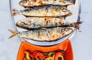 Prato com quatro sardinhas grelhadas e uma taça com pimentos salteados.