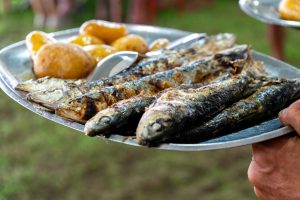 Prato metálico com sardinhas grelhadas e batatas servido num ambiente exterior em Ílhavo.