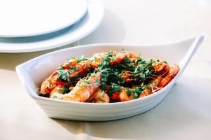 Travessa branca com camarões salteados decorados com ervas frescas e pequenos pedaços de pimento.