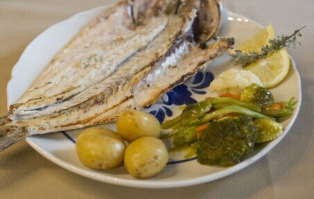 Prato com robalo grelhado, batatas cozidas, legumes verdes e laranja, e uma rodela de limão.