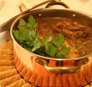 Panela de cobre com pedaços de carne estufada em molho castanho, decorada com salsa fresca por cima.