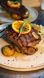 Bife de novilho grelhado servido com fatia de laranja, alecrim e batatas assadas.