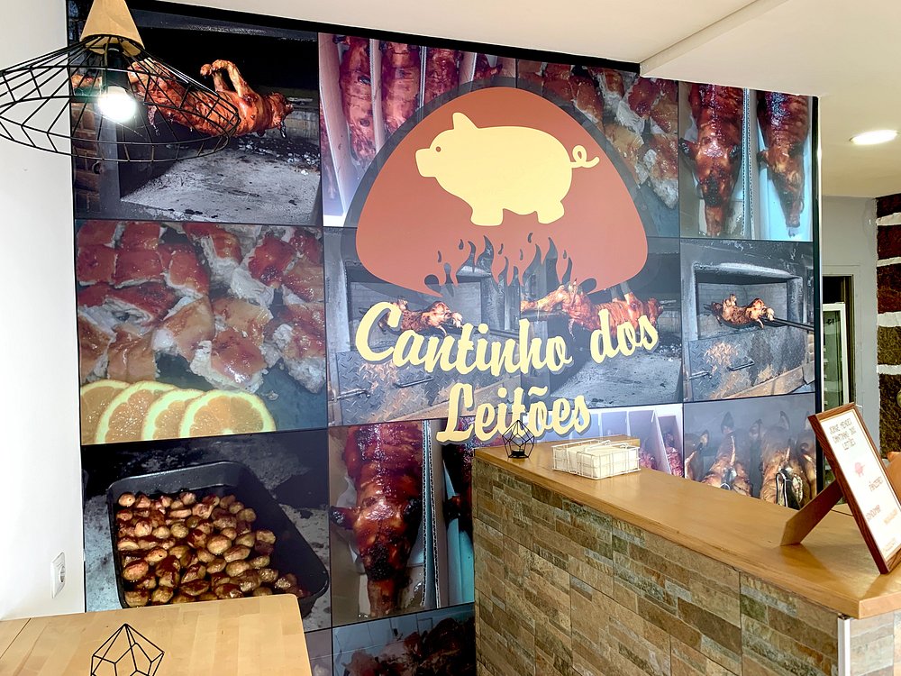 Parede com logótipo estilizado de leitão e várias fotografias de pratos de leitão assado, junto a balcão de madeira.
