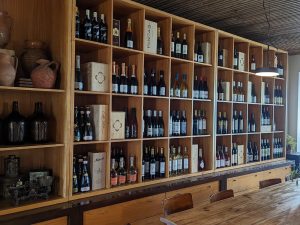 Garrafeira em madeira com garrafas de vinho, mesa comprida e cadeiras num ambiente iluminado.