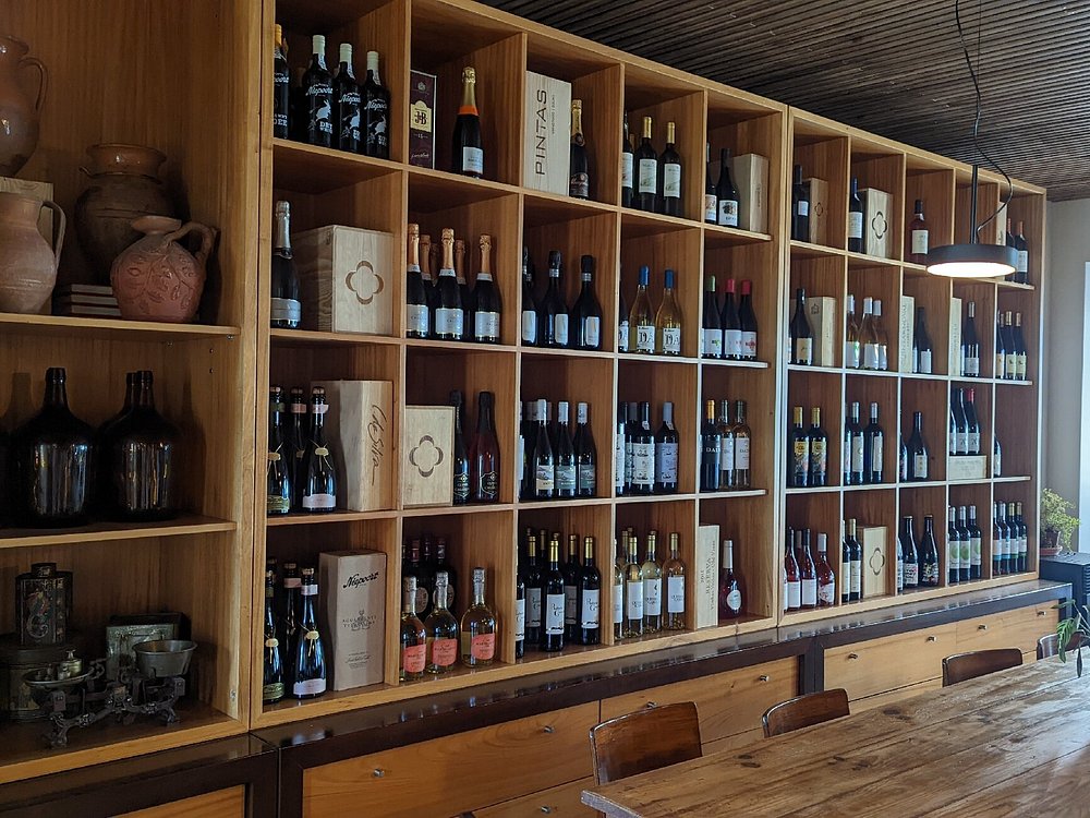 Garrafeira em madeira com garrafas de vinho, mesa comprida e cadeiras num ambiente iluminado.