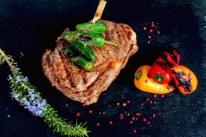 Bife grelhado com pimentos verdes por cima e pimentos assados ao lado, decorado com alecrim.