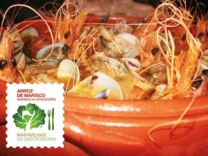 Tacho de barro com arroz de marisco, incluindo camarões, amêijoas e mexilhões; à esquerda vê‑se um rótulo com texto.