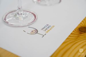 Logótipo “Vinhos & Sabores dos Altos” numa folha de prova com base de copo de vinho.