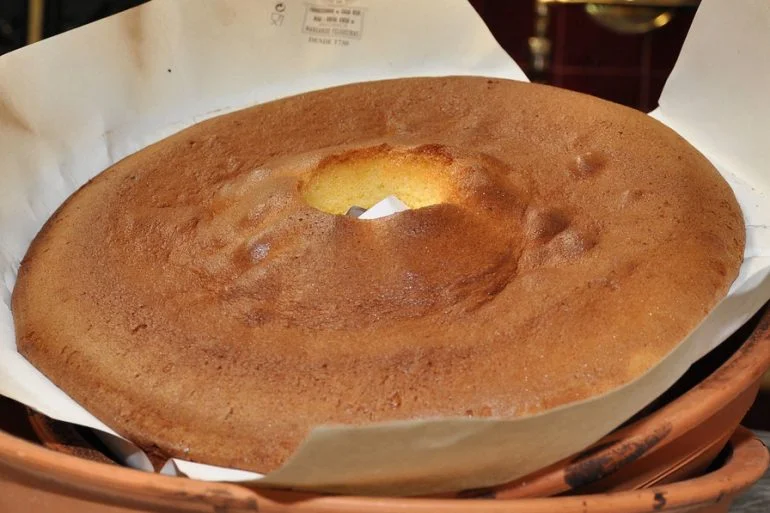 Pão de Ló grande e dourado colocado sobre papel vegetal dentro de uma forma de barro.
