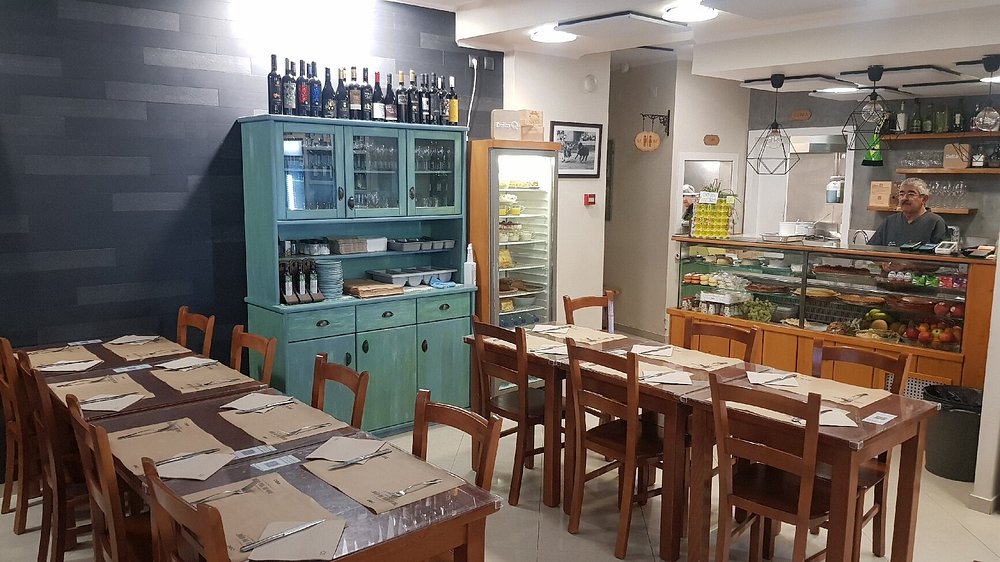 Sala com mesas de madeira preparadas, armário turquesa com garrafas e balcão com vitrine de alimentos.