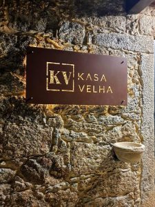 Placa metálica com o logótipo Kasa Velha fixada numa parede de pedra rústica.