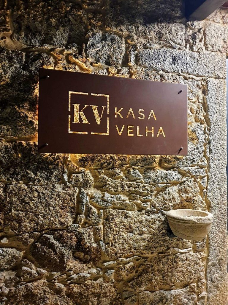 Placa metálica com o logótipo Kasa Velha fixada numa parede de pedra rústica.