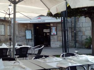 Esplanada com mesas postas, cadeiras escuras, guarda‑sóis brancos e toldo com o nome “Restaurante Chafariz”.