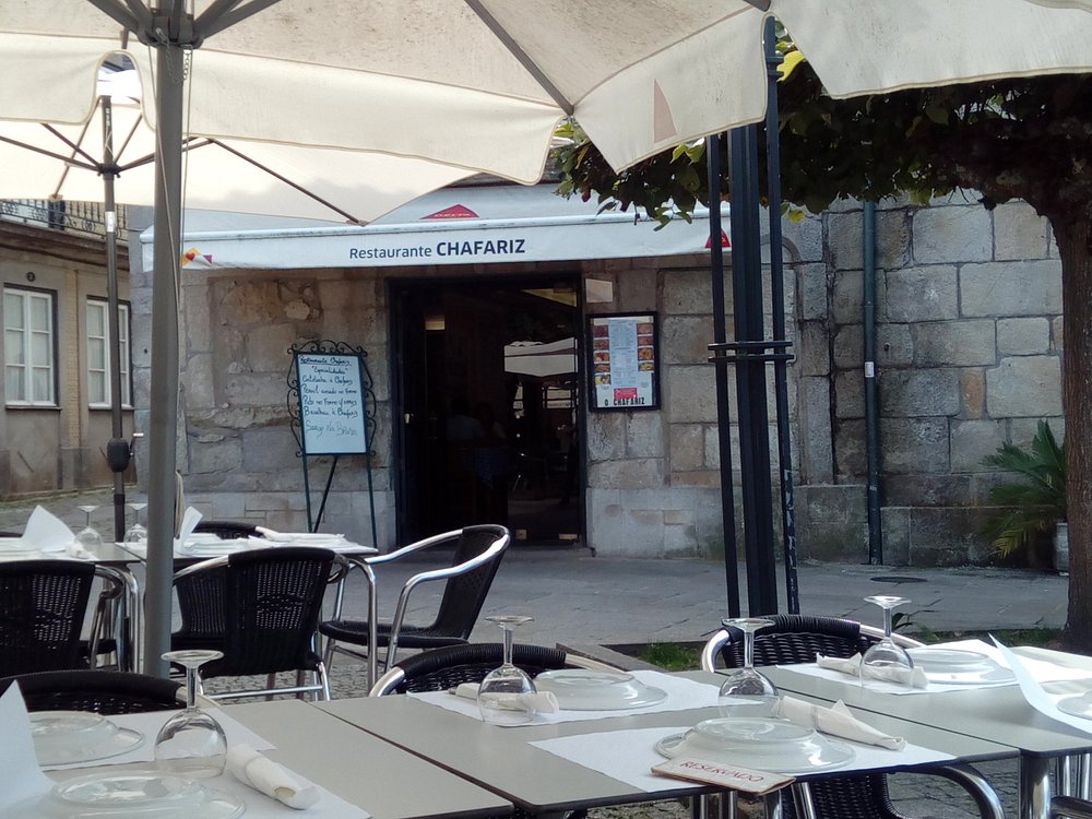 Esplanada com mesas postas, cadeiras escuras, guarda‑sóis brancos e toldo com o nome “Restaurante Chafariz”.