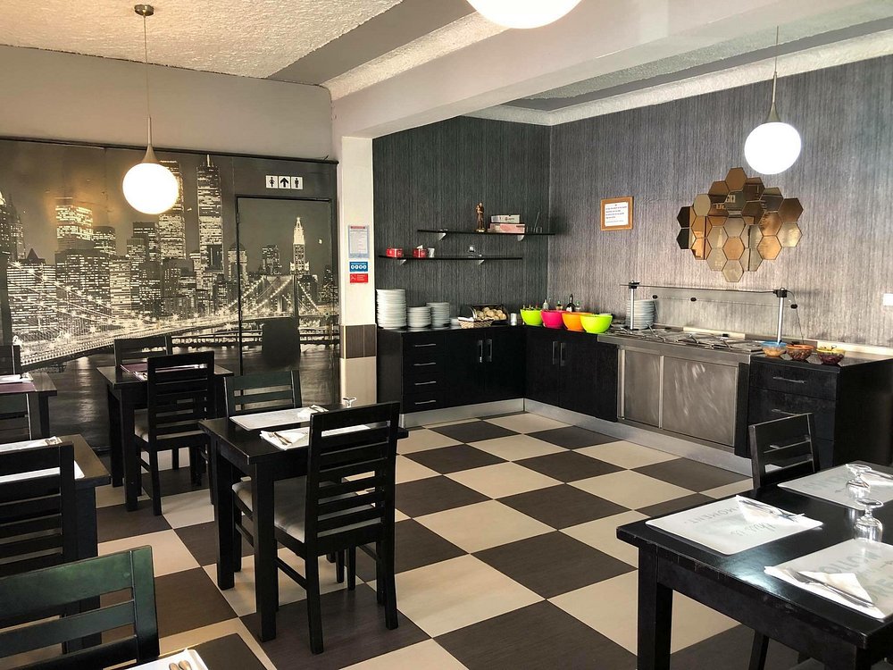 Sala com mesas arrumadas, chão em padrão xadrez e zona de buffet com loiça colorida e decoração moderna.