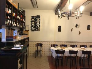 Interior de restaurante com mesa redonda preparada para refeição e garrafeira em madeira com garrafas expostas.