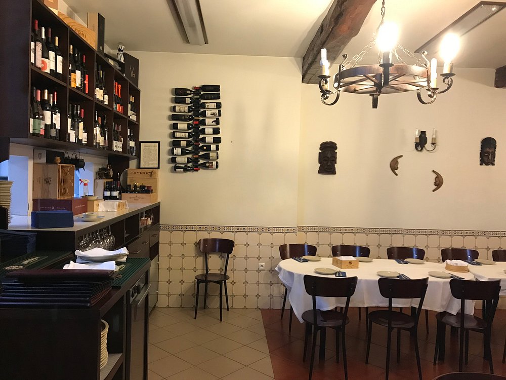 Interior de restaurante com mesa redonda preparada para refeição e garrafeira em madeira com garrafas expostas.