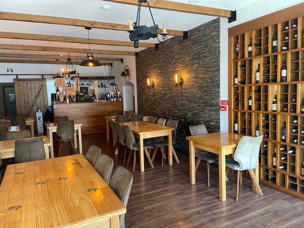 Interior de restaurante com mesas de madeira, garrafeira, balcão e iluminação quente.