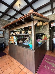 Balcão de madeira com telhado de telha, cestos pendurados, plantas e elementos decorativos num ambiente rústico.