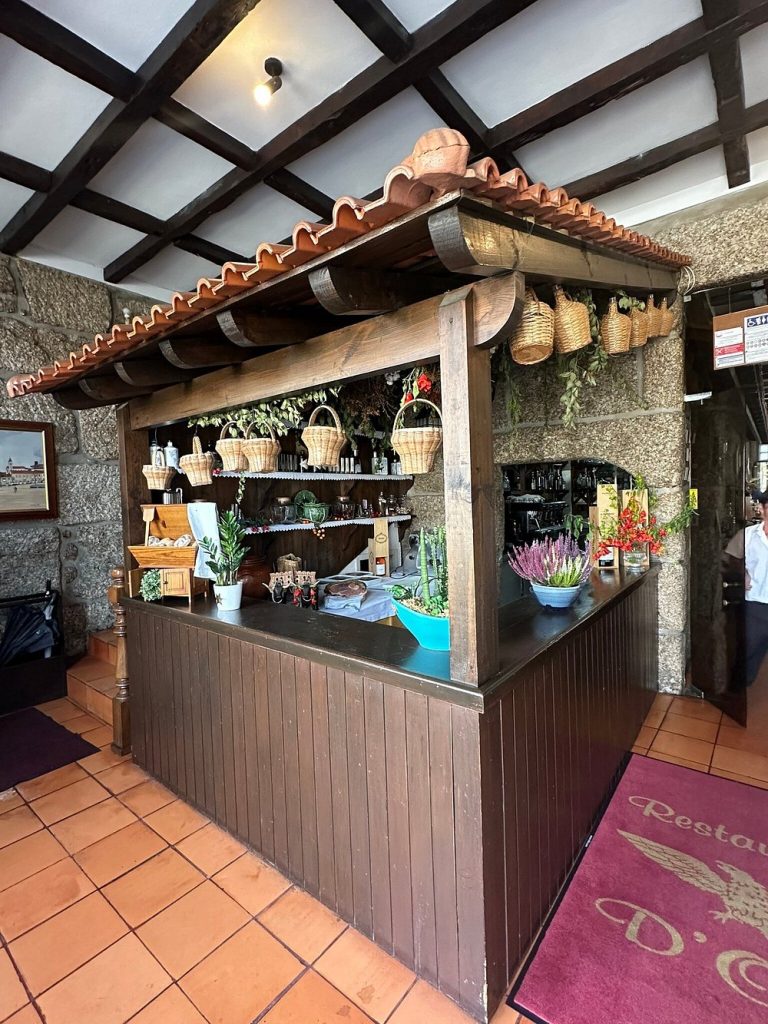 Balcão de madeira com telhado de telha, cestos pendurados, plantas e elementos decorativos num ambiente rústico.