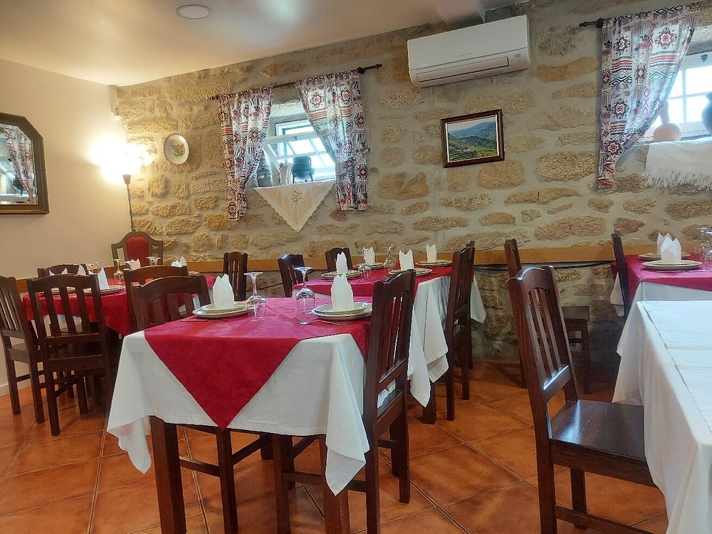 Sala de restaurante com mesas cobertas por toalhas brancas e passadeiras vermelhas, cadeiras de madeira e paredes em pedra com elementos decorativos.