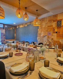 Sala de restaurante com mesas postas, toalhas claras e paredes revestidas com caixas de vinho em madeira.