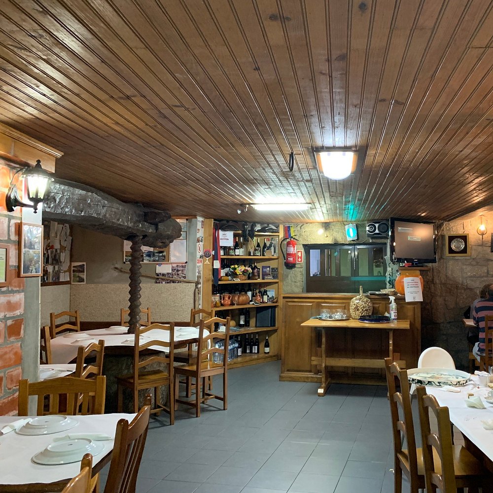 Sala com mesas cobertas por toalhas brancas, bar em madeira, paredes de pedra e tijolo.