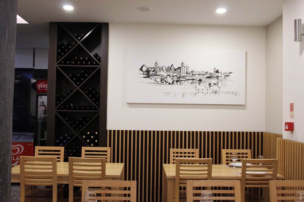 Sala de restaurante com mesas de madeira preparadas, copos de vinho e garrafeira alta com garrafas expostas.