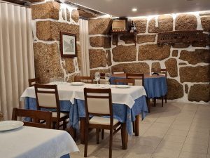 Sala com mesas cobertas por toalhas azuis e brancas, paredes de pedra e elementos decorativos rústicos.