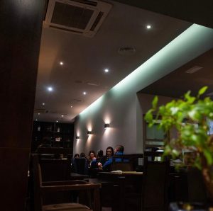 Interior do restaurante com mesas ocupadas, iluminação suave e decoração moderna.