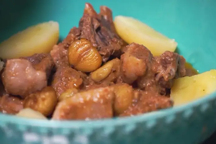Taça azul‑turquesa com carne estufada em molho castanho e batatas cozidas ao redor.