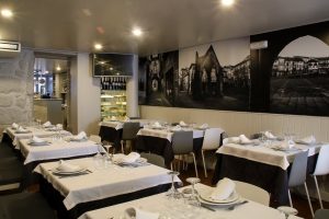 Sala de restaurante com mesas cobertas por toalhas brancas, cadeiras modernas e mural a preto e branco na parede.