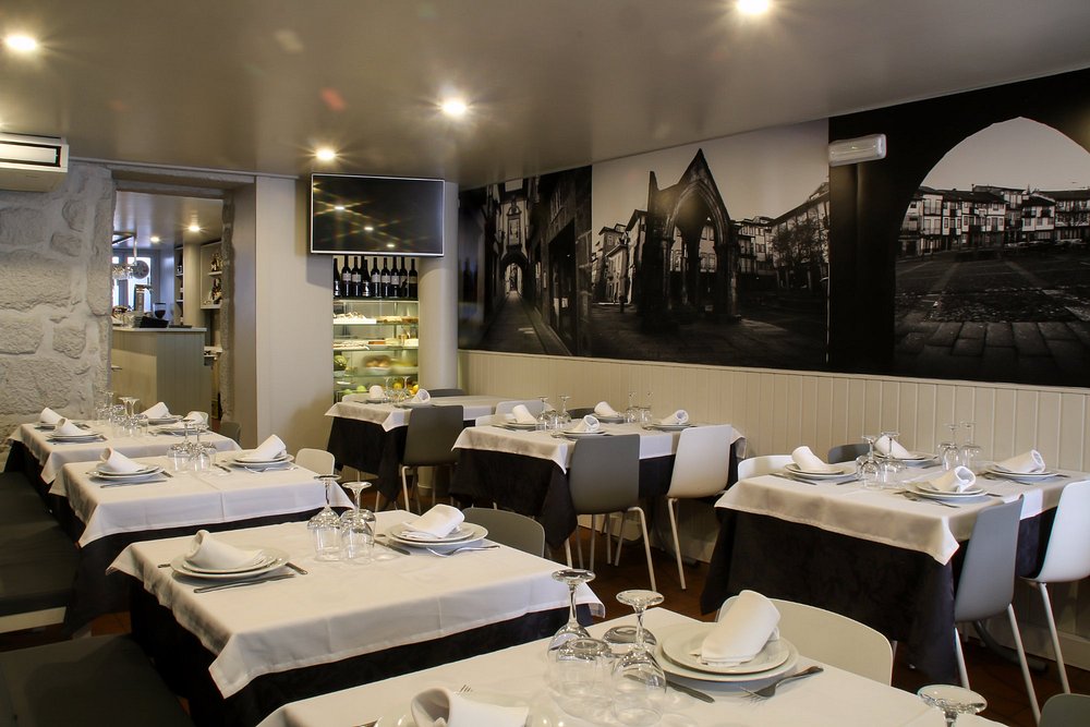 Sala de restaurante com mesas cobertas por toalhas brancas, cadeiras modernas e mural a preto e branco na parede.