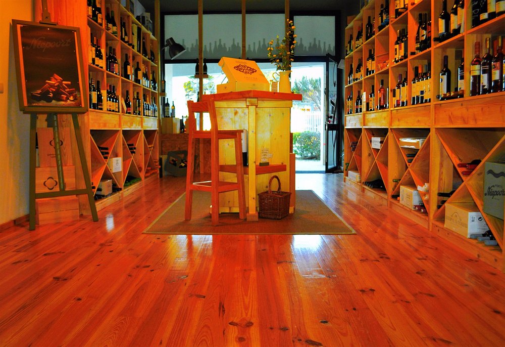 Sala com prateleiras de madeira cheias de garrafas de vinho, mesa central e portas de vidro ao fundo.