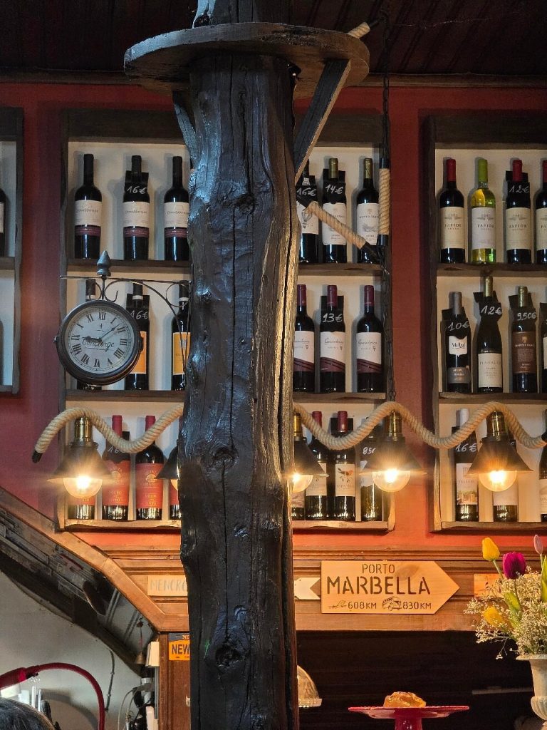 Prateleiras com garrafas de vinho com etiquetas de preço, iluminação quente, relógio antigo e decoração rústica.