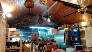 Interior rústico da Tasquinha do João com balcão, garrafas de vinho, decoração tradicional e iluminação quente.