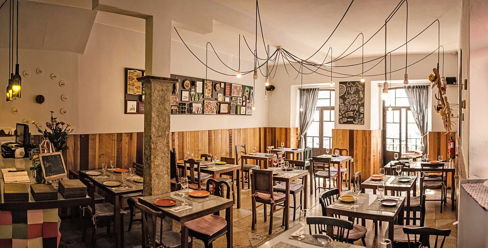 Sala de restaurante com mesas postas, cadeiras variadas, paredes com madeira e quadros, e iluminação suspensa.