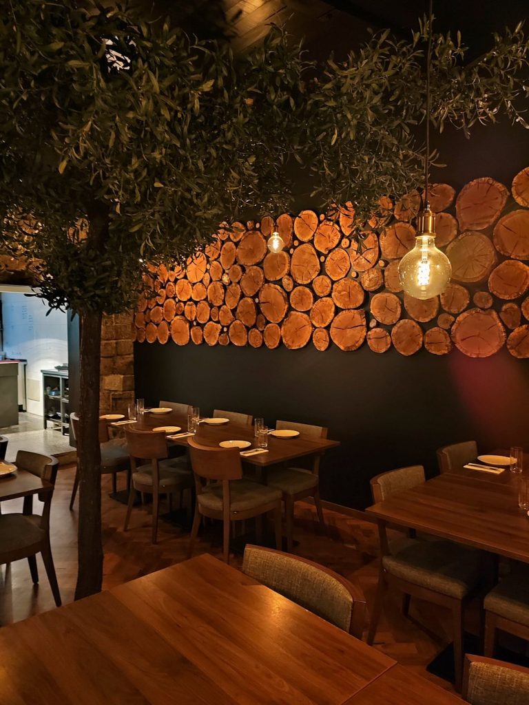 Sala de restaurante com mesas em madeira, luzes suspensas e parede decorada com círculos de madeira.