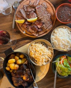 Mesa com pratos de carne grelhada, arroz simples e misto, feijão, batatas e salada.