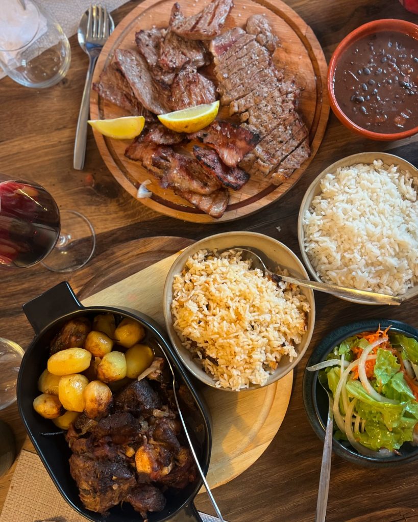 Mesa com pratos de carne grelhada, arroz simples e misto, feijão, batatas e salada.