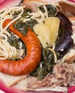 Prato com enchidos, carne cozinhada, massa, legumes verdes e pão.