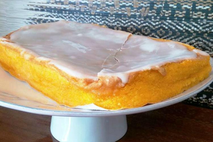 Bolinhol retangular com massa amarela e cobertura branca rachada sobre prato de pé.