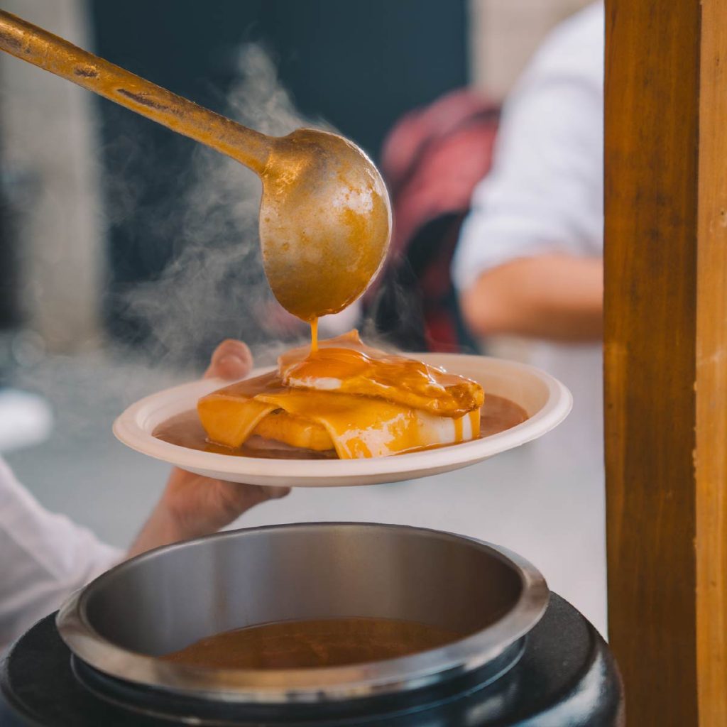 Mão a servir molho quente e espesso com uma concha sobre um prato com queijo derretido.