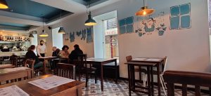 Interior do restaurante O Bairro em Aveiro, com mesas de madeira, iluminação pendente e ilustrações azuis nas paredes.