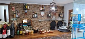 Balcão de restaurante com parede de pedra, garrafas de vinho e bebidas, frascos de conservas e pequenos pratos de petiscos sobre o balcão.