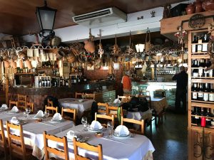 Interior rústico do restaurante com mesas postas, balcão em madeira e decoração tradicional nas paredes e teto.