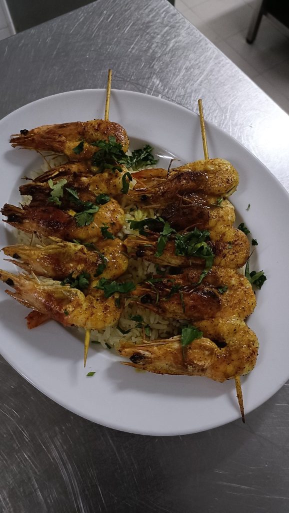 Espetadas de camarão grelhado colocadas sobre arroz branco num prato oval.