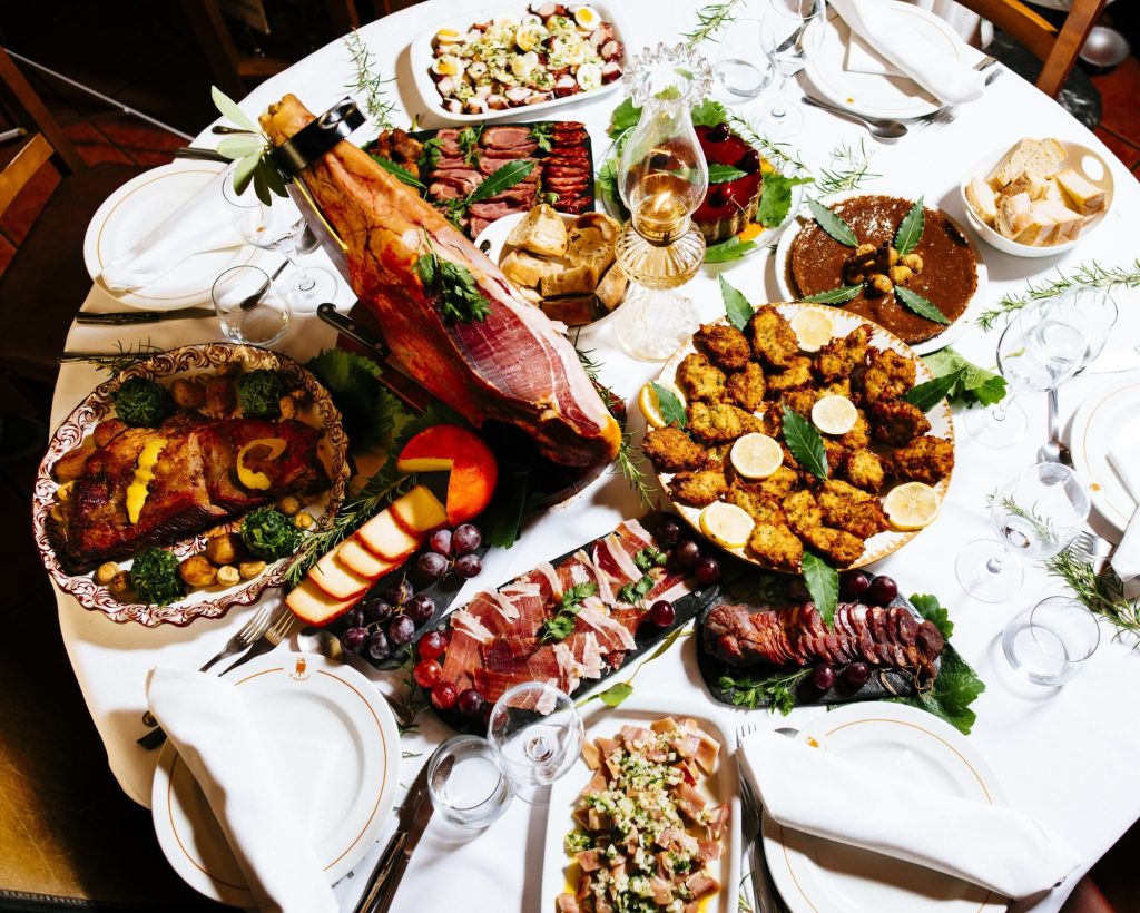 Mesa com presunto em suporte, enchidos, queijos, fritos, uvas e pão.