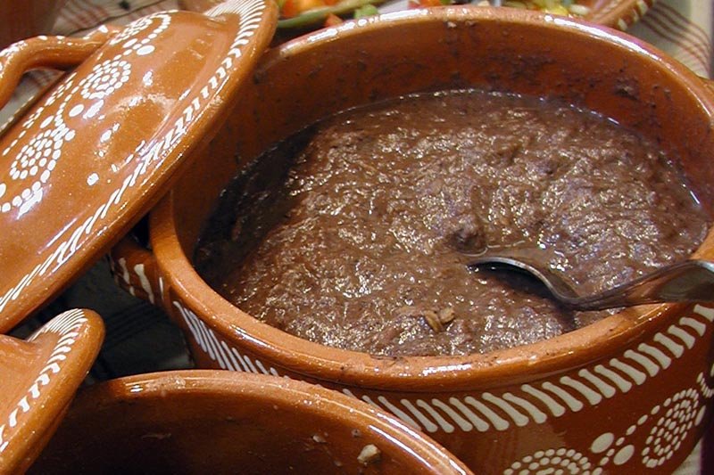 Panela de barro decorada com feijão cremoso e colher metálica no interior.
