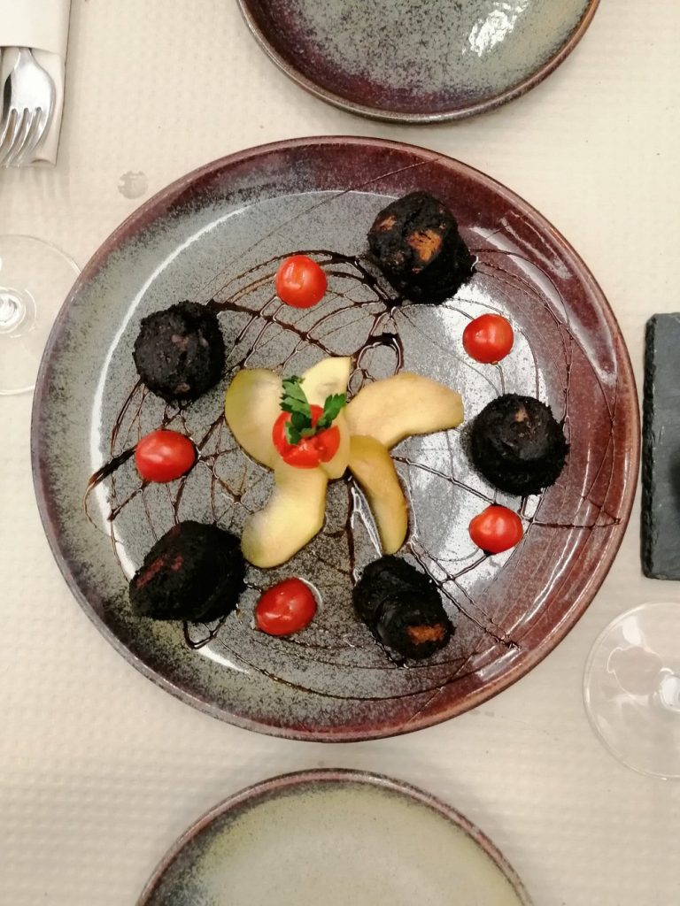 Prato redondo com peças de carne, fruta laminada no centro, tomate e fios de molho escuro.